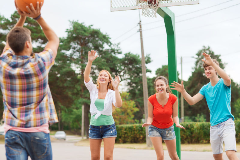 group of smiling teenagers playing basketball in a park