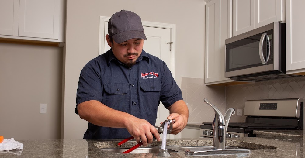 friendly parker & sons plumbing technician working on a customer's kitchen sink faucet