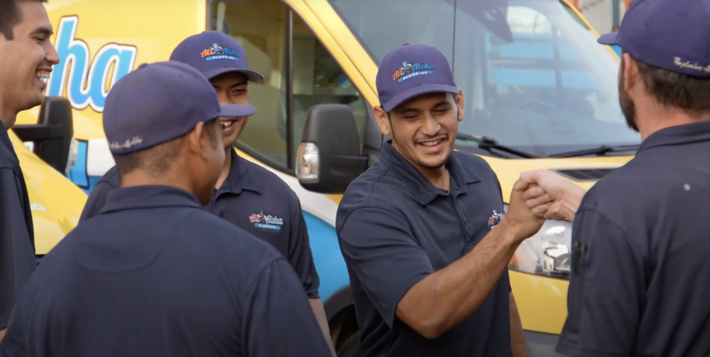 friendly team of All Aloha plumbers standing in a huddle next to their branded van