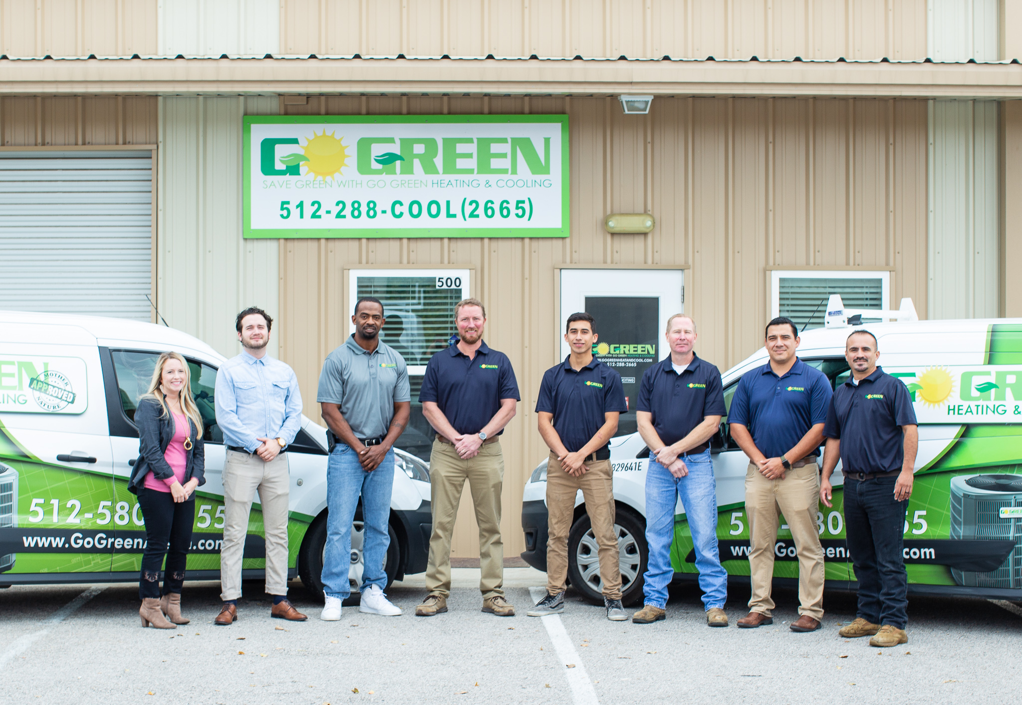 go green heating and cooling employees posing for a picture outside their office, in front of branded company vans