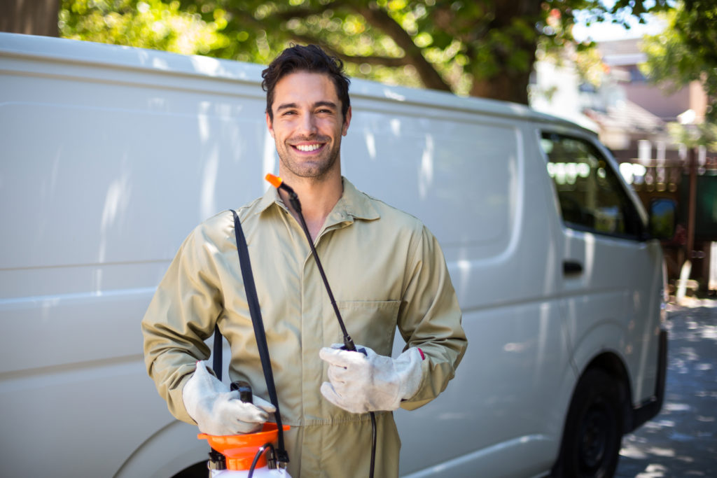 friendly pest control techinican wearing a beige protective suit, holding a treatment sprayer